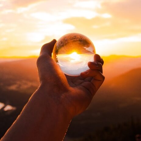 hand holding glass globe with sunset shining through